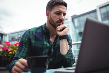 Poster - Businessman using laptop while having a cup of coffee