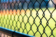 View through chain link fence from inside dugout with baseball field blurred in background