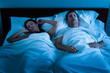 Sleeping man with obstructive sleep apnea snoring loudly in bed while tortured wife plugs her ears
