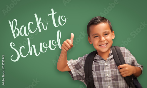 Cute Hispanic Boy With Thumbs Up Wearing A Backpack In Front of Chalk Board w...