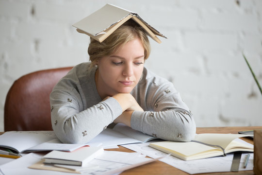 Portrait of a student girl at the desk with an open book on her head, education concept photo, lifestyle