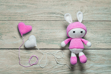 Wall Mural - crochet bunny toy on a wooden background with balloons in the form of hearts on wooden background, top view. congratulatory concept.