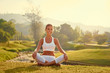 © Loginova - Yoga at park with view of the mountains, with sunlight. Young woman in lotus pose sitting on green grass. Concept of calm and meditation.