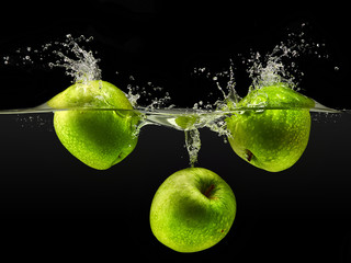 Group of green apples falling in water on black background