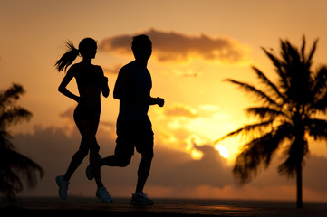 Couple man and woman running jogging silhouettedagainst tropical sunrise sunset with palm trees and ocean on South Miami Beach Florida