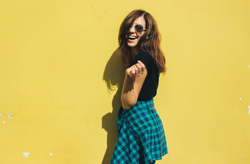 Brunette girl in rock black style, standing against yellow wall outdoors in the city street