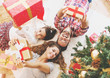© Tijana - Family gather around a Christmas tree, holding presents