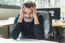 Mature Man Sitting In Office With Head In Hands