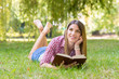Smiling beautiful young woman lying on grass and reading book