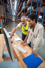 Warehouse manager and worker discussing with computer 