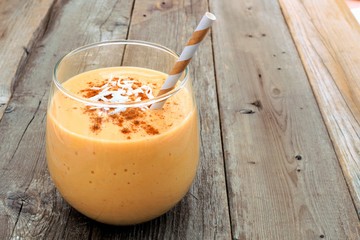 Wall Mural - pumpkin smoothie with coconut and cinnamon in a tumbler glass against a rustic wood background