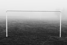 Black And White Image Of Soccer Football Goal Posts In Empty Field Pitch In Winter Fog