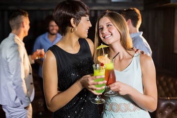 Wall Mural - Female friends holding glass of cocktail in bar