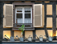 Window On The Facade Of A Half-timbered House With Open Shutters And Watering Cans, Standing On The Windowsill.
