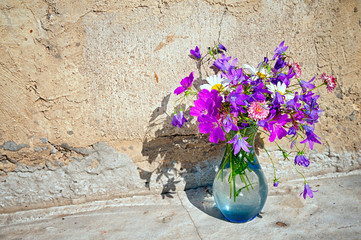 Wall Mural - Bouquet of wild flowers - bluebells, daisies, clover against the background of a concrete wall with copy space foe your text