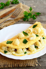 Wall Mural - Omelet stuffed with cauliflower and parsley on a plate, fork, knife, burlap on an old wooden table. Diet breakfast recipe. Vintage style