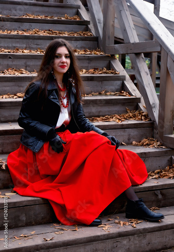Fotografija Young dark-haired woman in a black leather jacket and a bright beads sits liftin