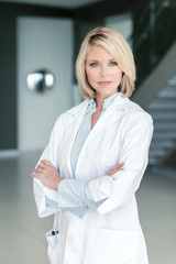 Attractive blond female woman doctor psychiatrist therapist in medical office with arms crossed