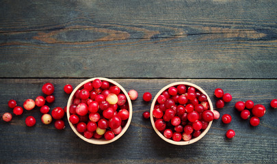 Fresh juicy cranberry in wooden round bowls with a wooden spoon on a table, top view