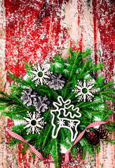 Wall Mural - Christmas fir branches on rustic red wooden background.Vintage Christmas wooden toy in the form of a deer. Handmade wooden snowflakes. Spruce cones. The red ribbon in the cage.