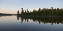 Trees On The Shoreline Reflected In The Tranquil Lake; Lake Of The Woods, Ontario, Canada