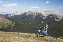 A Weather Station On Top Of A Ridge With Mountains And Valley In The Distance And Blue Sky With Clouds; Alberta, Canada