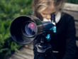 Beautiful blond girl in a school uniform in the park looking through  telescope