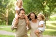 © mimagephotos - Happy young parents carrying kids and walking in park