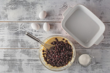 Whole-wheat flour in white bowl, milk, eggs on a light wooden ba