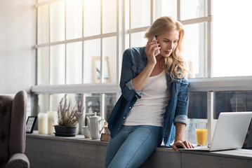 Blond woman talking per mobile phone near window