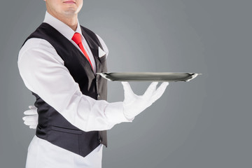 Handsome young waiter in gloves and red cravat holding empty tray