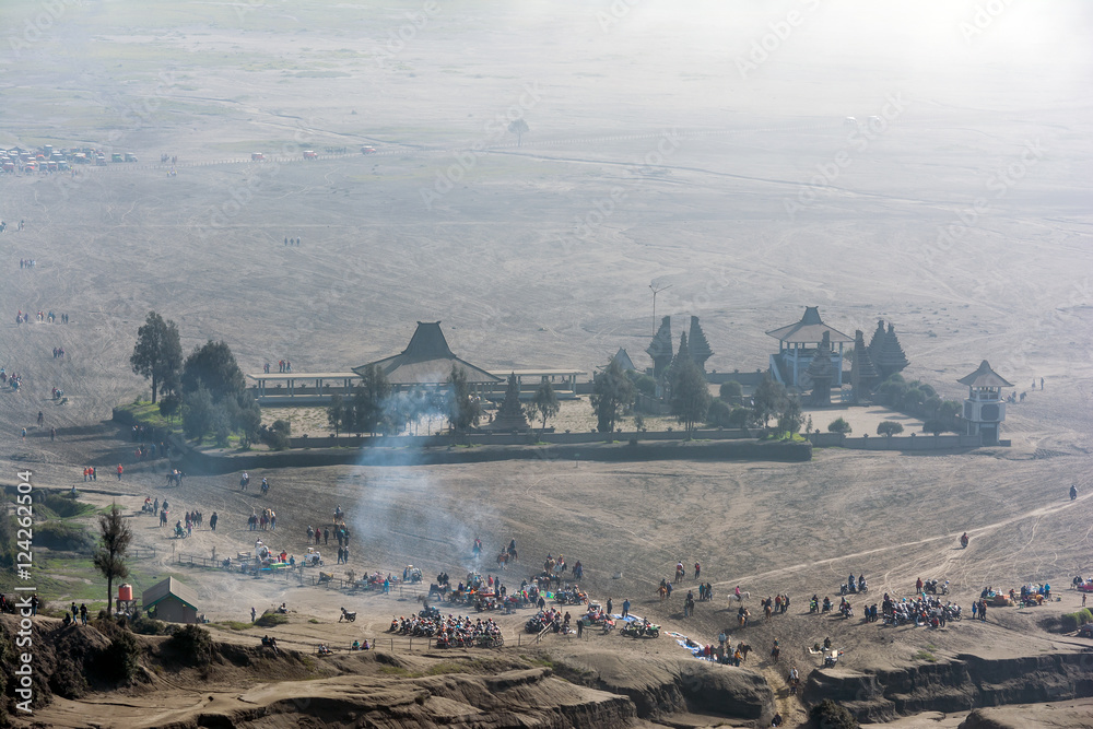 Looking down at the misty morning of caldera sea-sand plain from Mount Bromo. Tourist can be seen flocking around taking selfies, walking and horseback riding along the route to volcano crater.

 - obrazy, fototapety, plakaty 