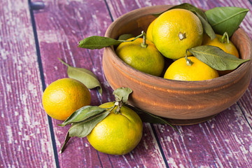  Tangerines.   Ripe tangerines with sprigs in a wooden bowl and on an old wooden table.