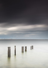 Wooden Posts In A Row In The Shallow Water Along The Coast With A View Of A City In The Distance Under Dark Storm Clouds;St. Mary's Bay Northumberland England