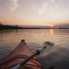 Bow Of A Red Kayak And Paddle On A Tranquil Lake At Sunset;Keewatin Ontario Canada