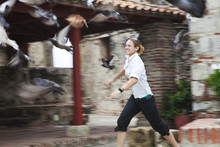 A Young Woman Runs After A Flock Of Birds Taking Flight; Cartagena, Columbia