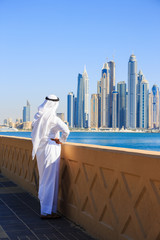 Wall Mural - Arab man in national dress looks at the city of Dubai