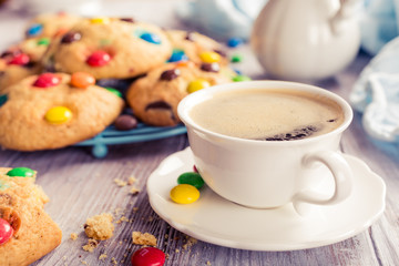 Wall Mural - Cup coffee with homemade cookies with colorful chocolate candies on old white wooden table. Retro style toned.