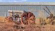 © AlessandraRC - Old white tractor rusting away in old farm equipment graveyard on very dry California grass, against steel wall
