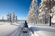 Sunny winter landscape with a man traveling Finnish Lapland with snowmobile