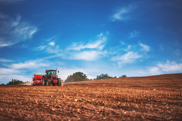 Farmer with tractor seeding crops at field