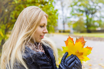 In cold autumn day woman with the colorful, beautiful maple leaves sitting on the bench in the park.