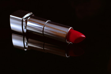 Red lipstick on mirroring table with black background.