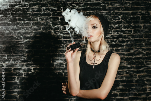 Sexy goth girl smokes electronic cigarette on dark background. The ...