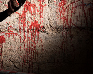 Blood stained wall and male hand holding a saw