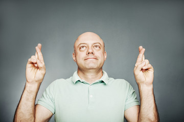 Closeup portrait hopeful man crossing her fingers, eyes closed,