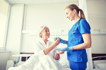 nurse giving medicine to senior woman at hospital