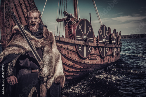 Viking warrior with sword standing near Drakkar on seashore Wallpaper Mural