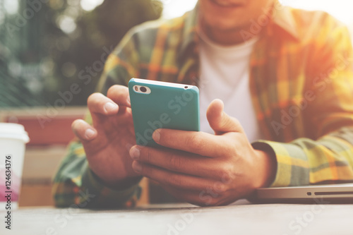 Fotografie, Obraz Young man with smartphone in hand sitting in street cafe, texting with friends