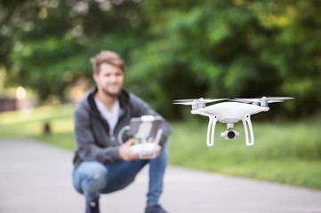 Young hipster man with flying drone. Sunny green nature.